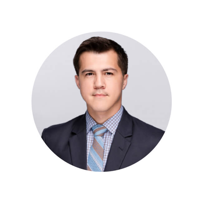 Professional headshot of Austin, a young man wearing a dark navy blazer, checked shirt, and striped blue tie.