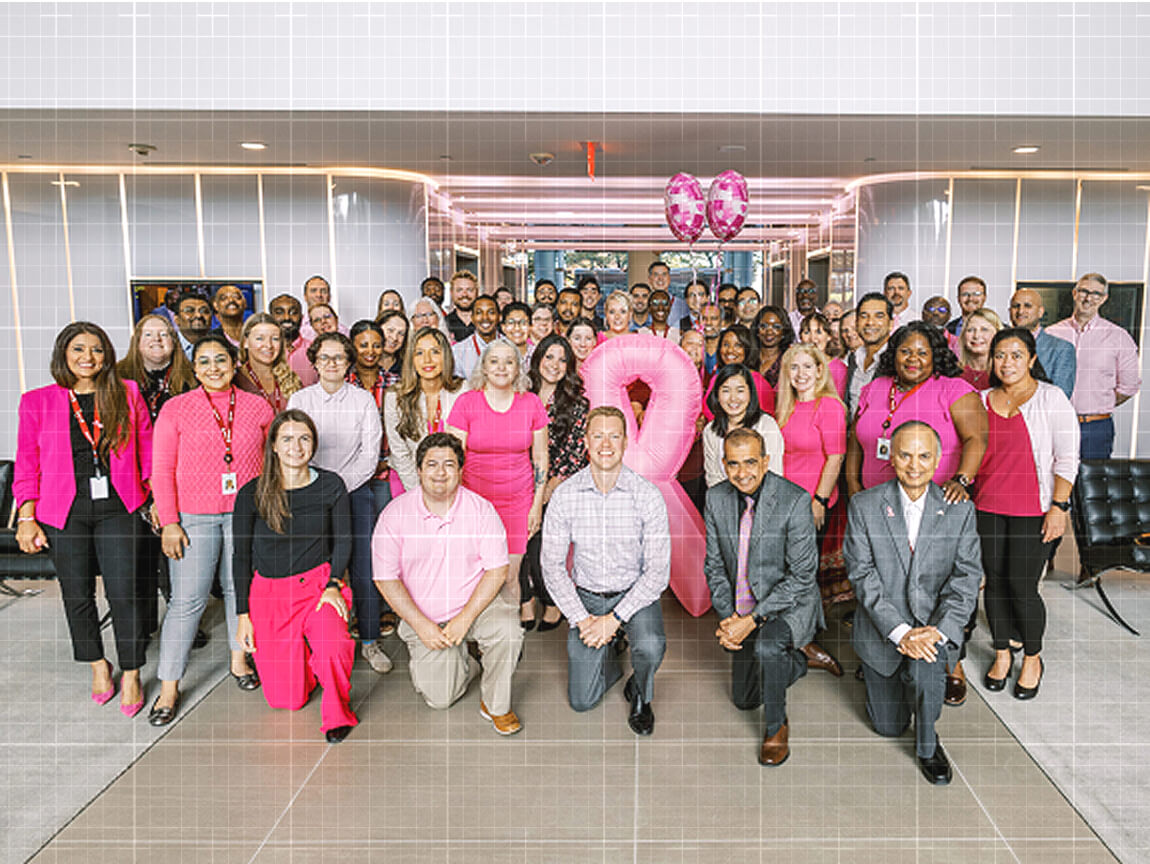 Credence team members wearing pink gather in an office lobby with pink balloons for a breast cancer awareness event.