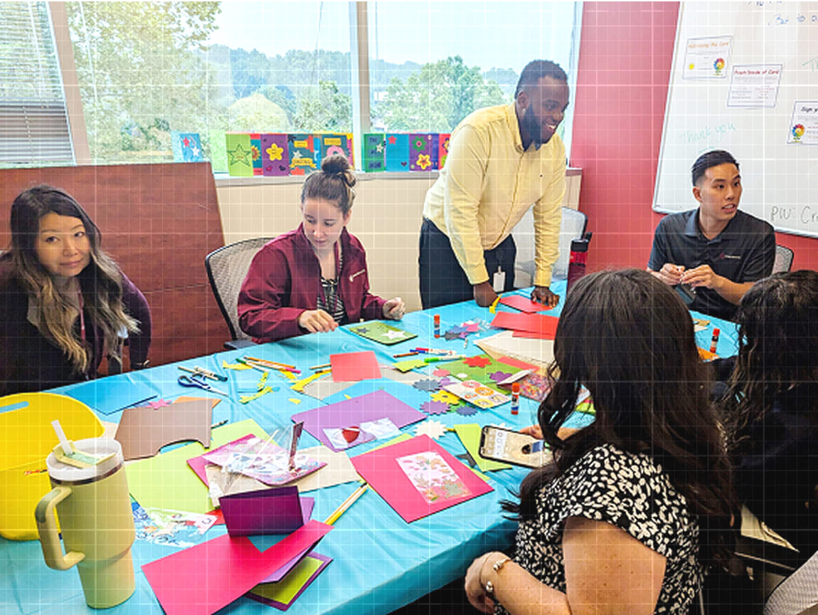 Credence team members gather around a table covered with colorful craft supplies to create handmade cards together.