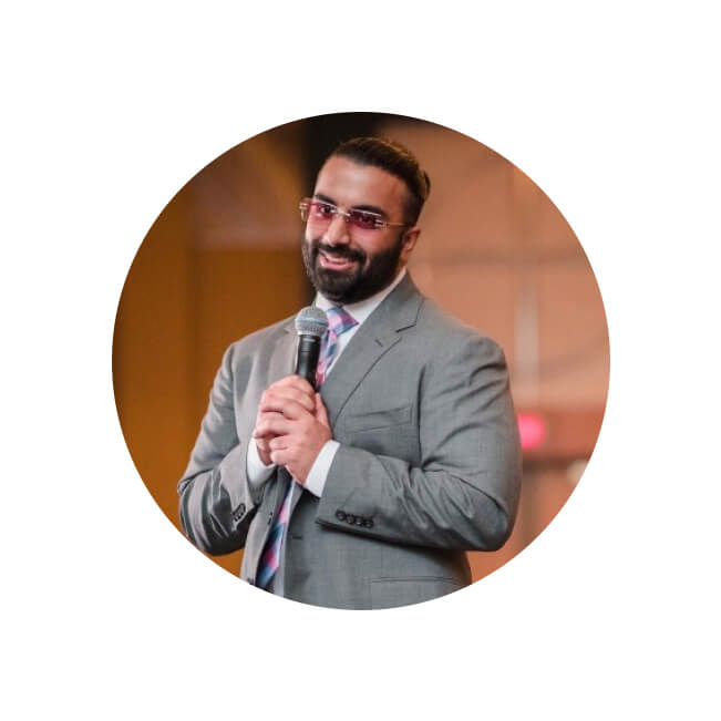 Vikram, a bearded man in a gray suit and tinted glasses, smiles while holding a microphone at a professional event.