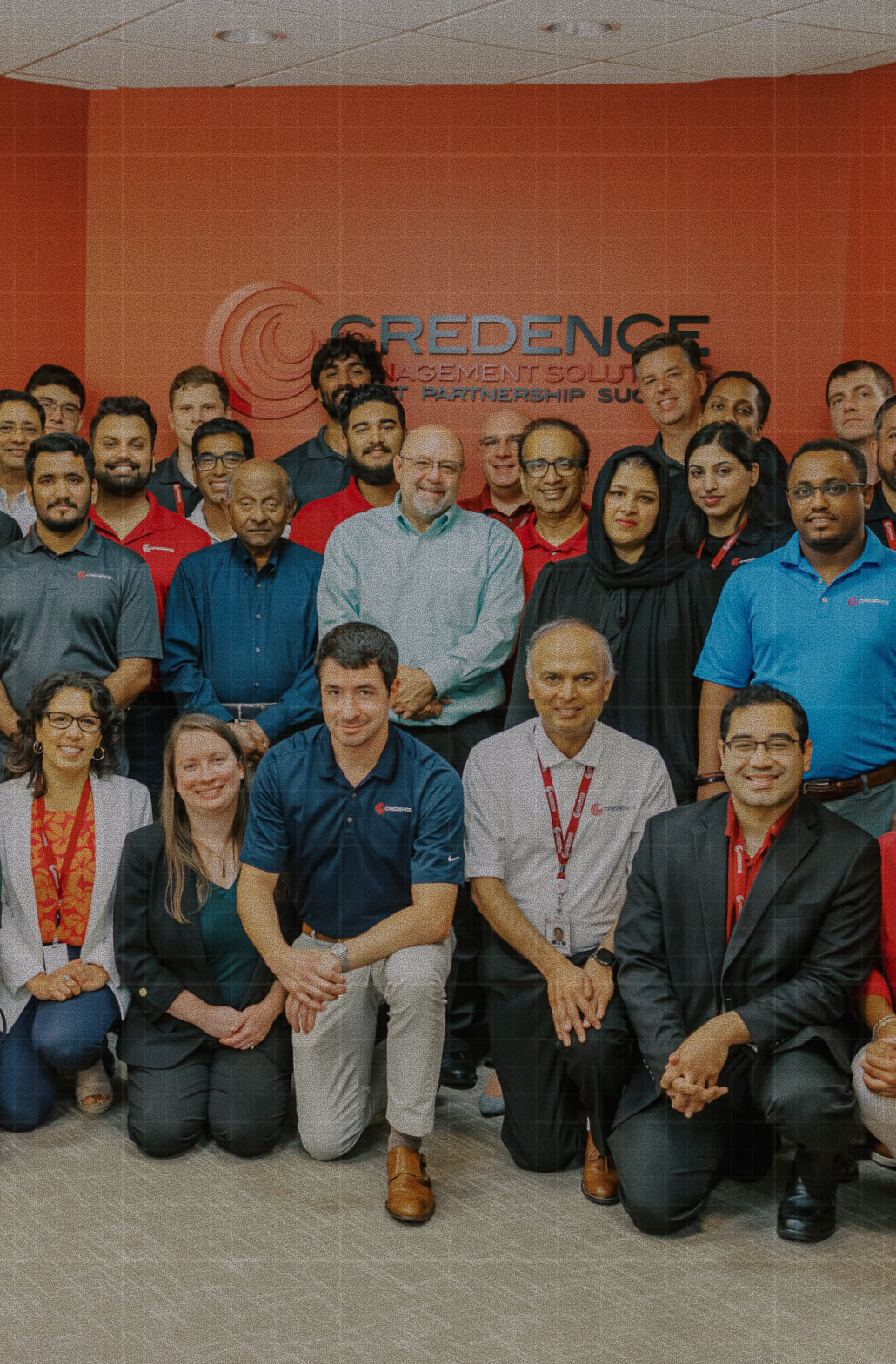 Credence Defined Culture Drives Results A diverse group of Credence Management Solutions employees poses together in front of the company's orange branded wall.