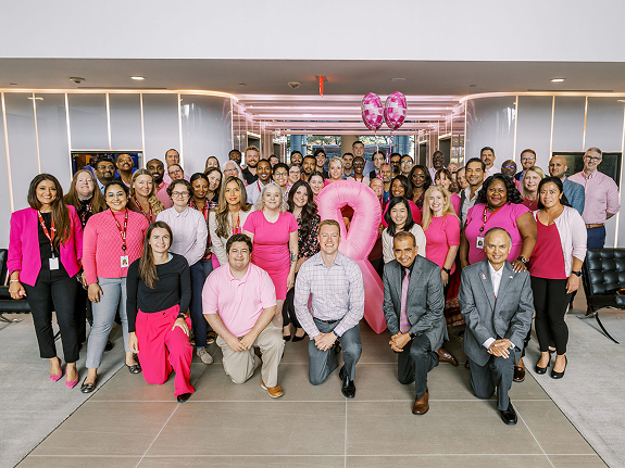 A large group of employees wearing pink poses together with pink balloons and decorations supporting the American Cancer