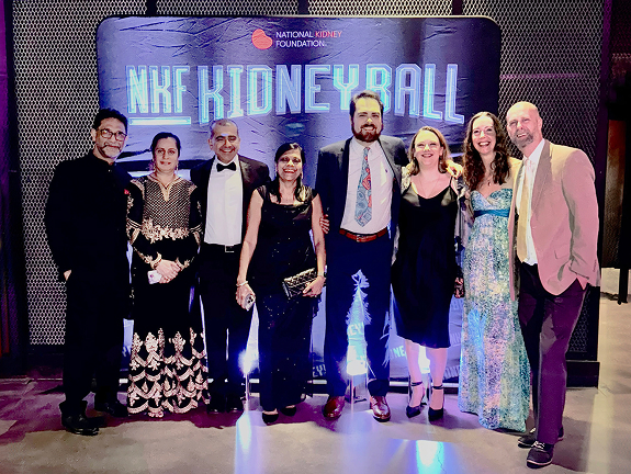 A group of eight formally dressed people posing together in front of an NKF Kidney Ball backdrop at a gala event.