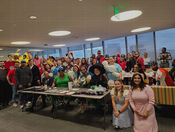 A large group of Credence team members in Halloween costumes poses together in a modern office during a festive celebration.