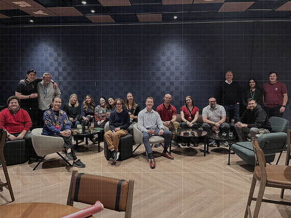 A group of approximately twenty Credence team members posing together in a modern lounge with dark walls and soft seating.