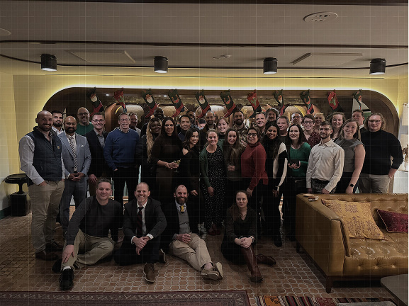 A large team poses together for a group photo in a festive office space decorated with holiday stockings.