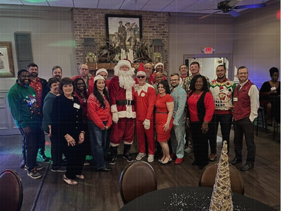 A team group photo at a holiday Christmas party with someone dressed as Santa Claus and festive holiday outfits.