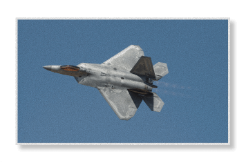 An F-22 Raptor stealth fighter jet banks sharply during flight against a clear blue sky, displaying its distinctive angular