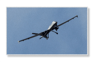 An MQ-9 Reaper unmanned aerial vehicle flies against a clear blue sky with its long slender wings and nose-mounted sensor